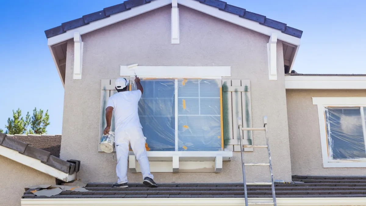 Painter masking a window during painting of plaster cladding on an exterior wall