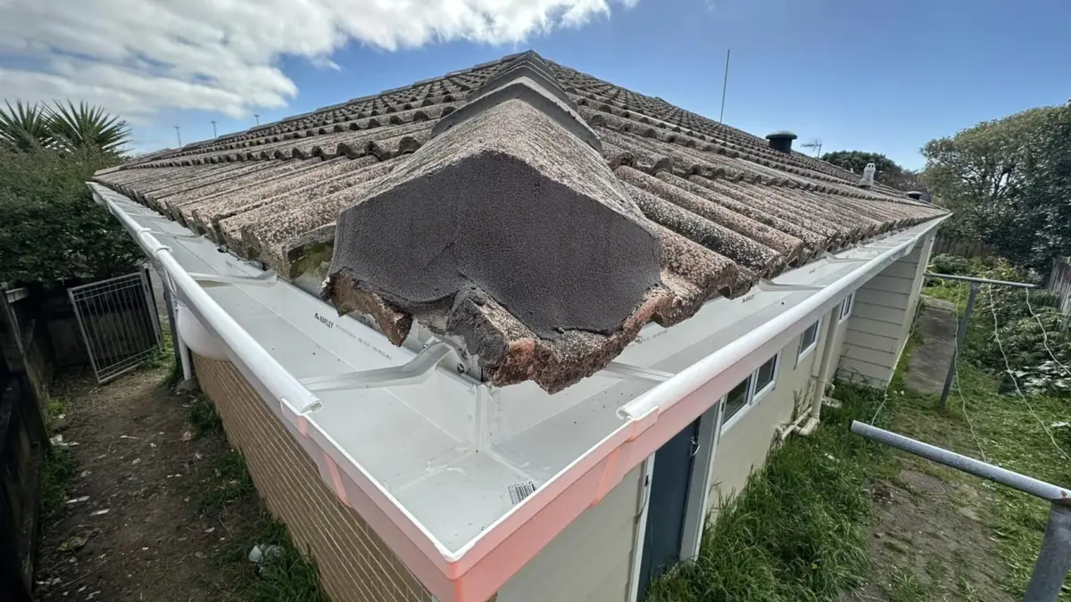 Damaged hip end of a tile roof, one of the roof leak causes, with felt over a broken ridge above a white gutter