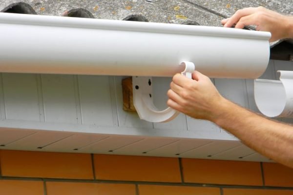 Contractor installing plastic roof gutter. Plastic guttering, rain guttering & drainage by handyman hands.